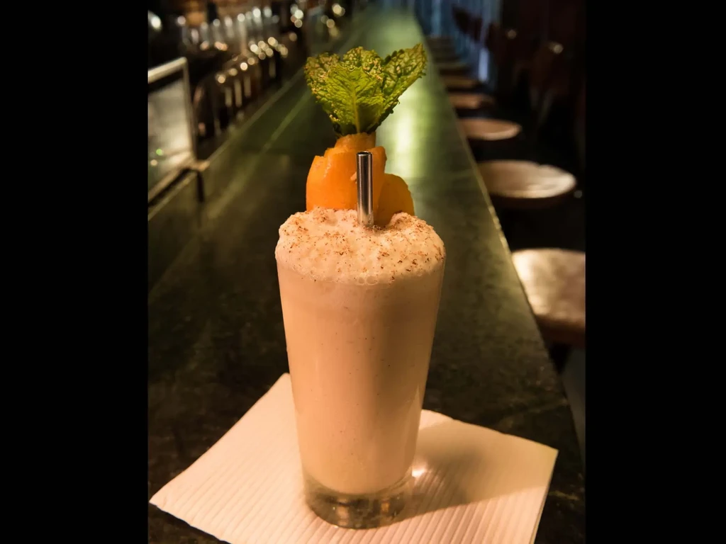 A tall drink with foam and garnish sits on a bar.