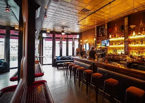 Dimly lit bar interior with a full bar, stools, and exposed brick.