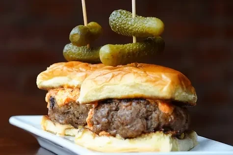Two sliders with pickles on top, served on a white plate.