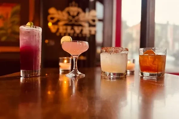 Four cocktails sit on a glossy wooden bar.