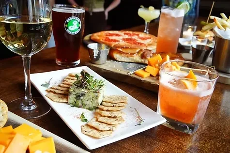 A table full of food, snacks, and drinks including cocktails and beer.