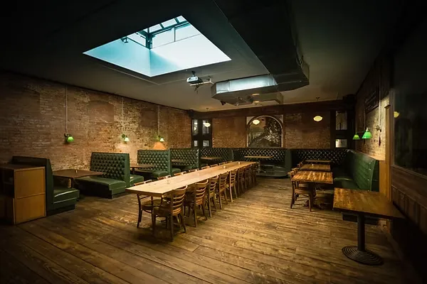 Restaurant with green booth seating, exposed brick, wood floors, and a skylight.