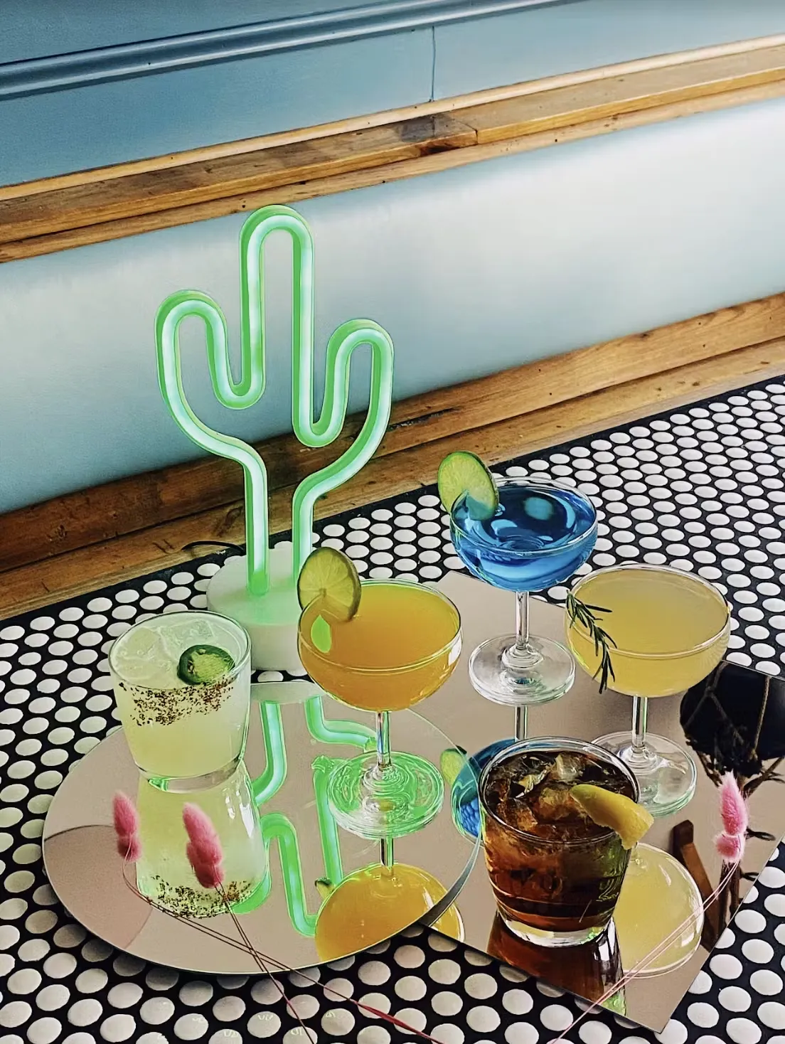 A neon cactus and cocktails on a mirrored tray and polka-dot surface.