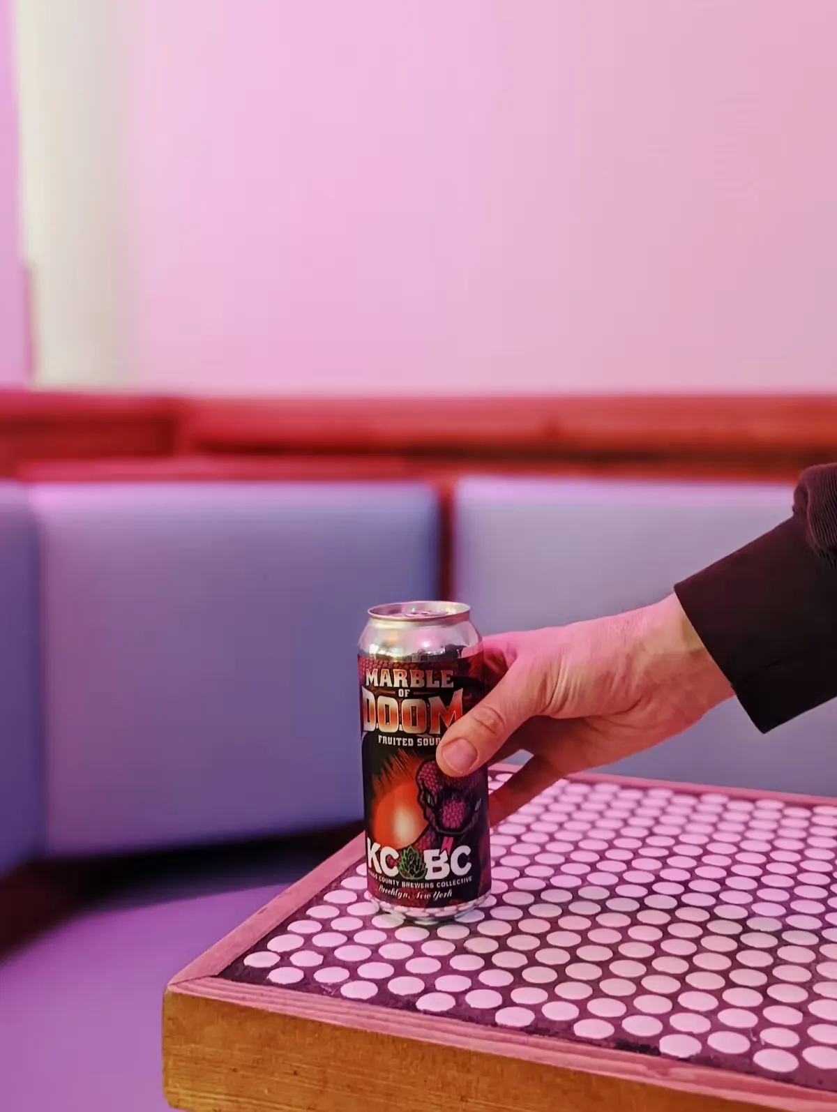 A hand places a can of "Marble of Doom" on a white polka dot table.