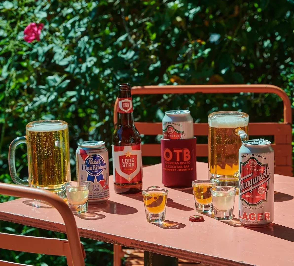 A picnic table with beer, shot glasses, and cans in an outdoor setting.