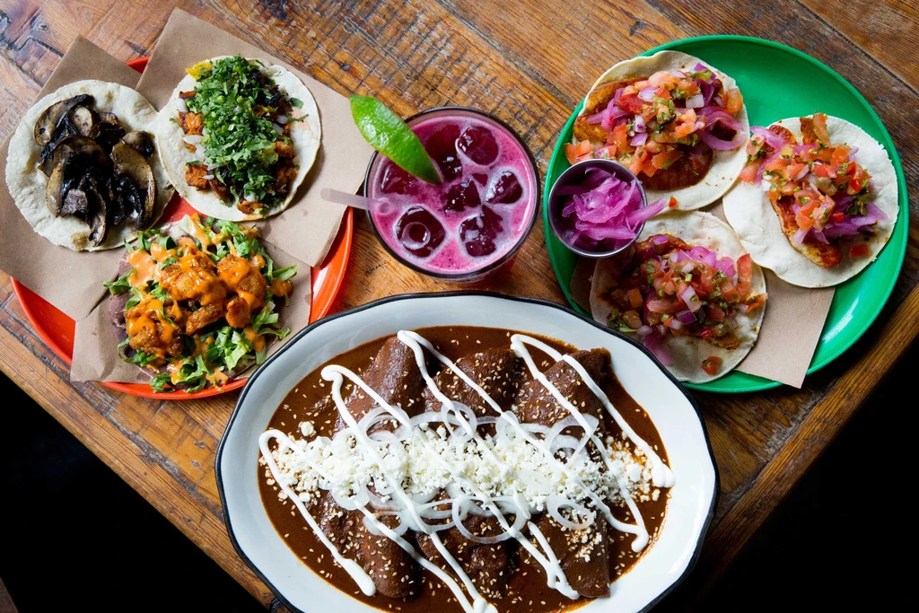 A table filled with tacos, enchiladas, and a pink drink.