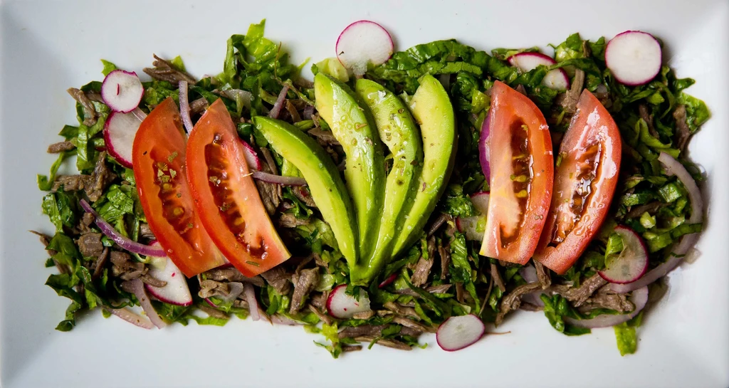 Platter of shredded beef salad with avocado, tomato, onion, and radish.