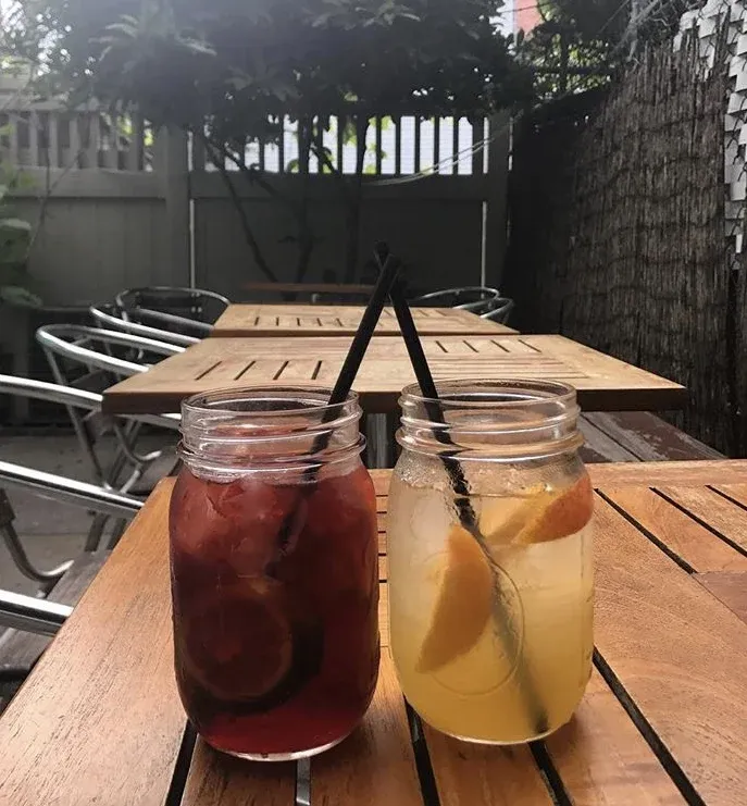 Two mason jars with drinks on a wooden patio table.