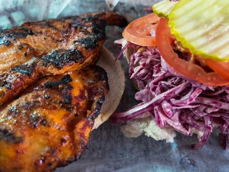 Close-up of a grilled chicken sandwich with purple coleslaw, tomato, and pickle.