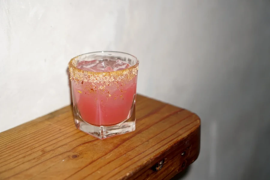 Pink drink in a glass with a coated rim on a wooden surface.
