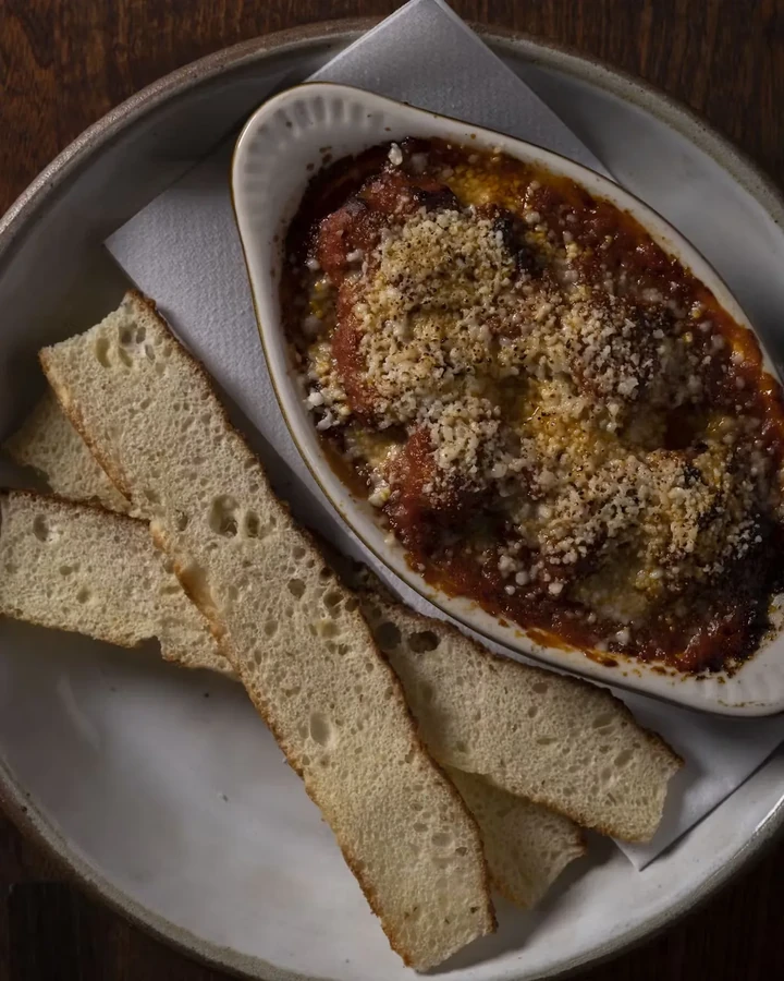 Baked red sauce dish with a breadcrumb topping, served with bread.