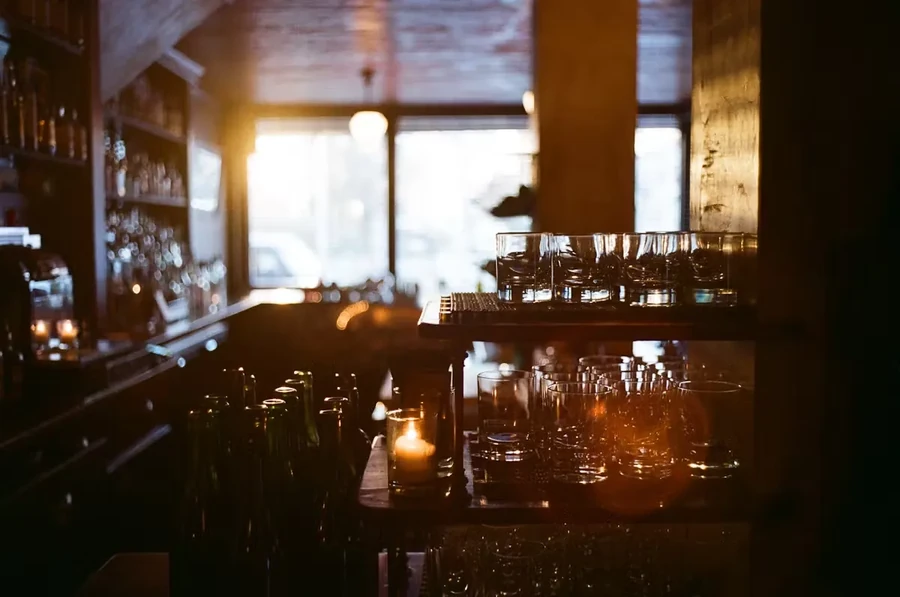 Warmly lit bar interior with rows of empty glasses and bottles.