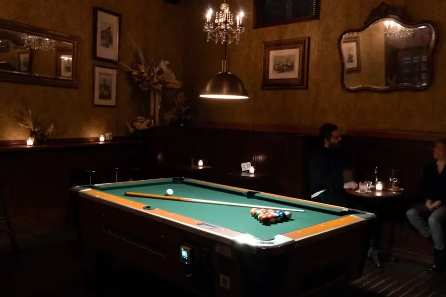 A dimly lit bar with a pool table and two people chatting.