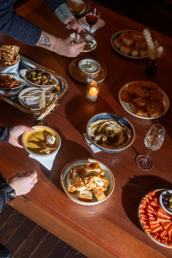 Hands serving small plates of appetizers, dips, and pastries on a table.