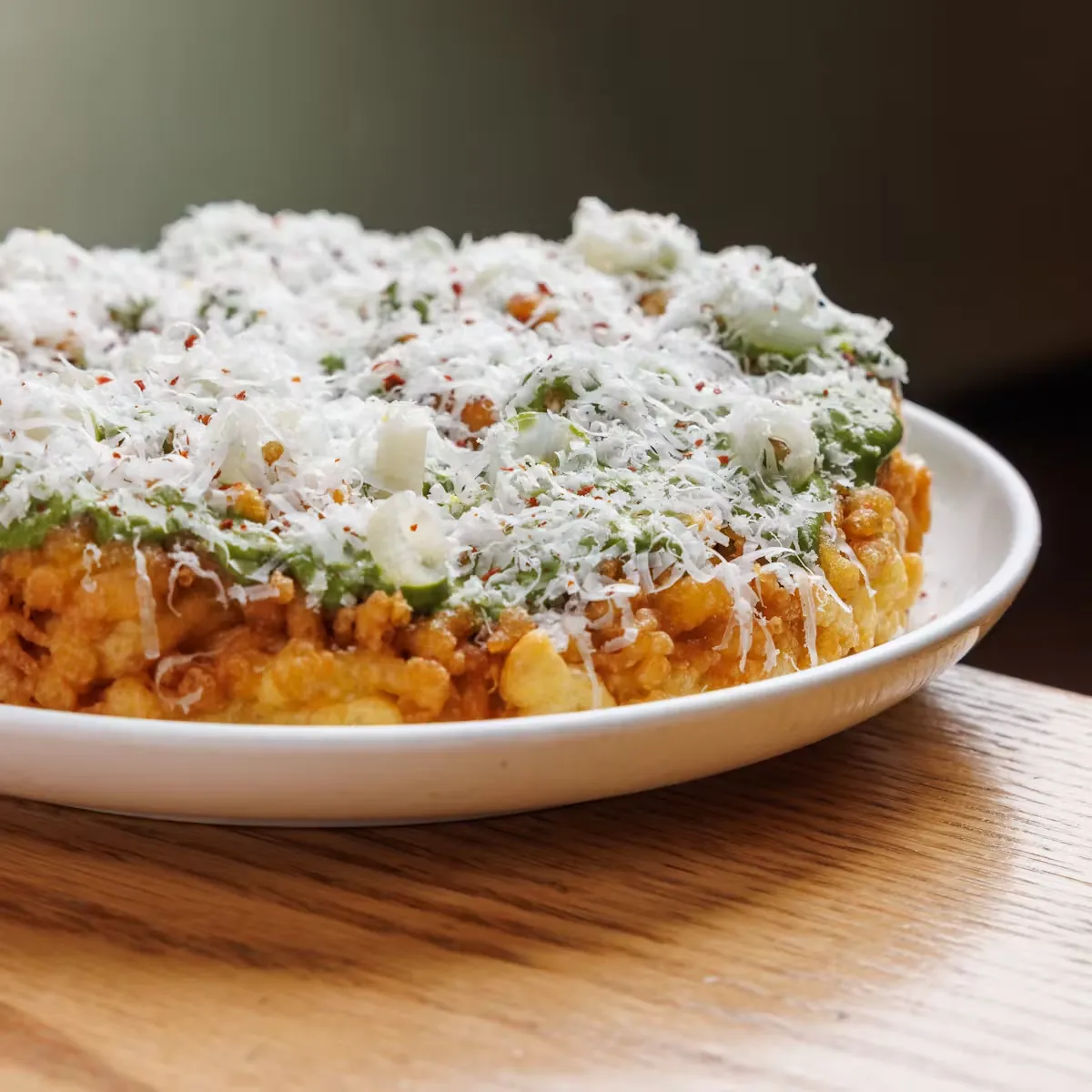 A round dish with green sauce, white cheese, and red flakes.