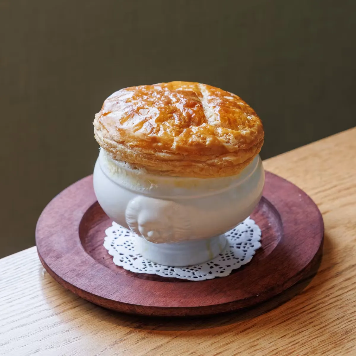 A white bowl with a golden puff pastry top on a wooden plate.