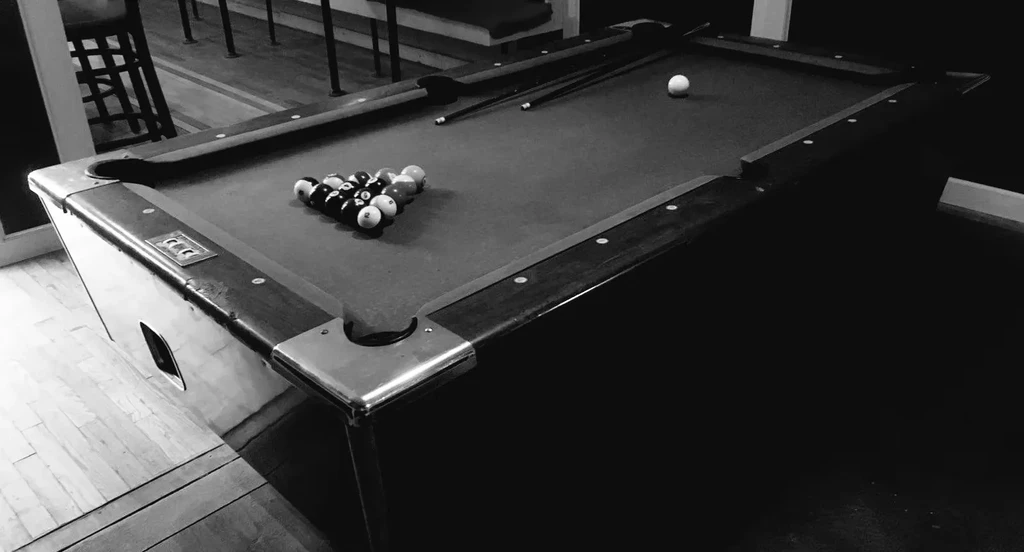 A black and white image of a pool table with racked balls.