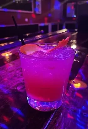 A bright pink cocktail with ice and an orange peel garnish.