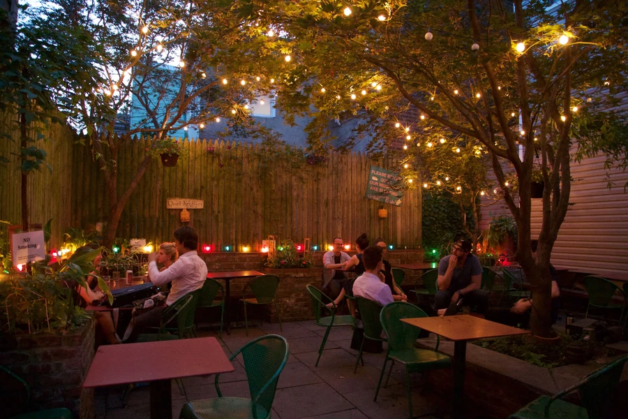 Outdoor patio at night with string lights, people seated at tables.