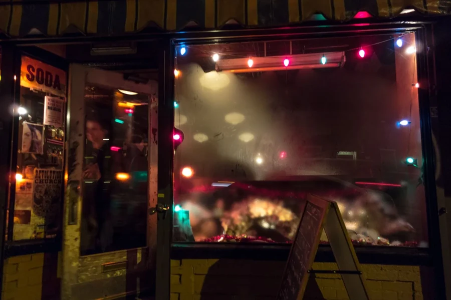 Storefront at night with SODA sign and colorful string lights.