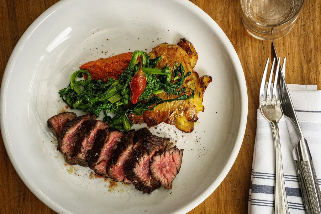 Sliced steak, roasted vegetables, and sauce on a white plate.
