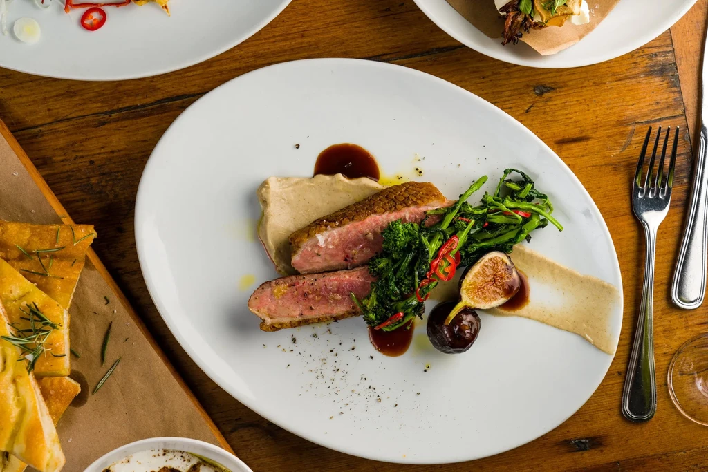 A duck breast dish with broccoli, fig, and puree on a white plate.
