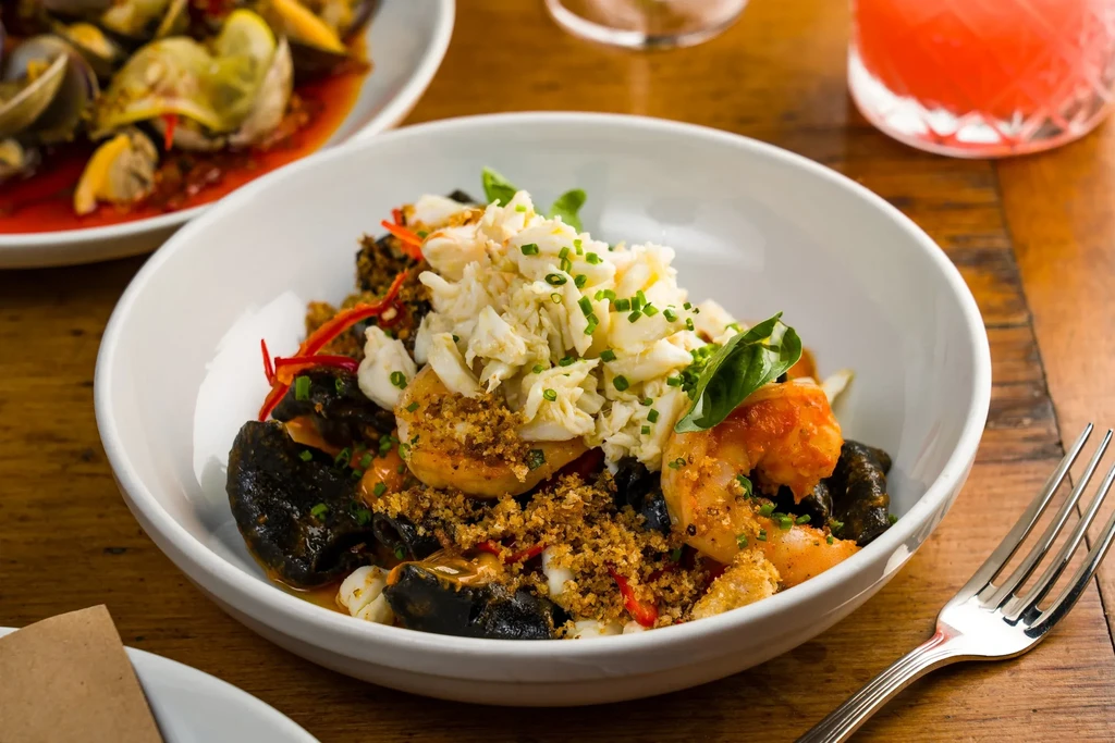 A white bowl of seafood pasta with shrimp and crab meat.