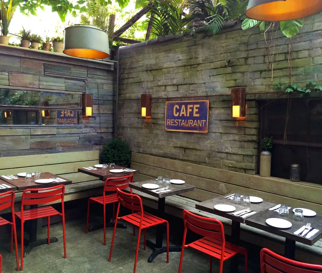 An empty outdoor cafe with red chairs and long wooden benches.