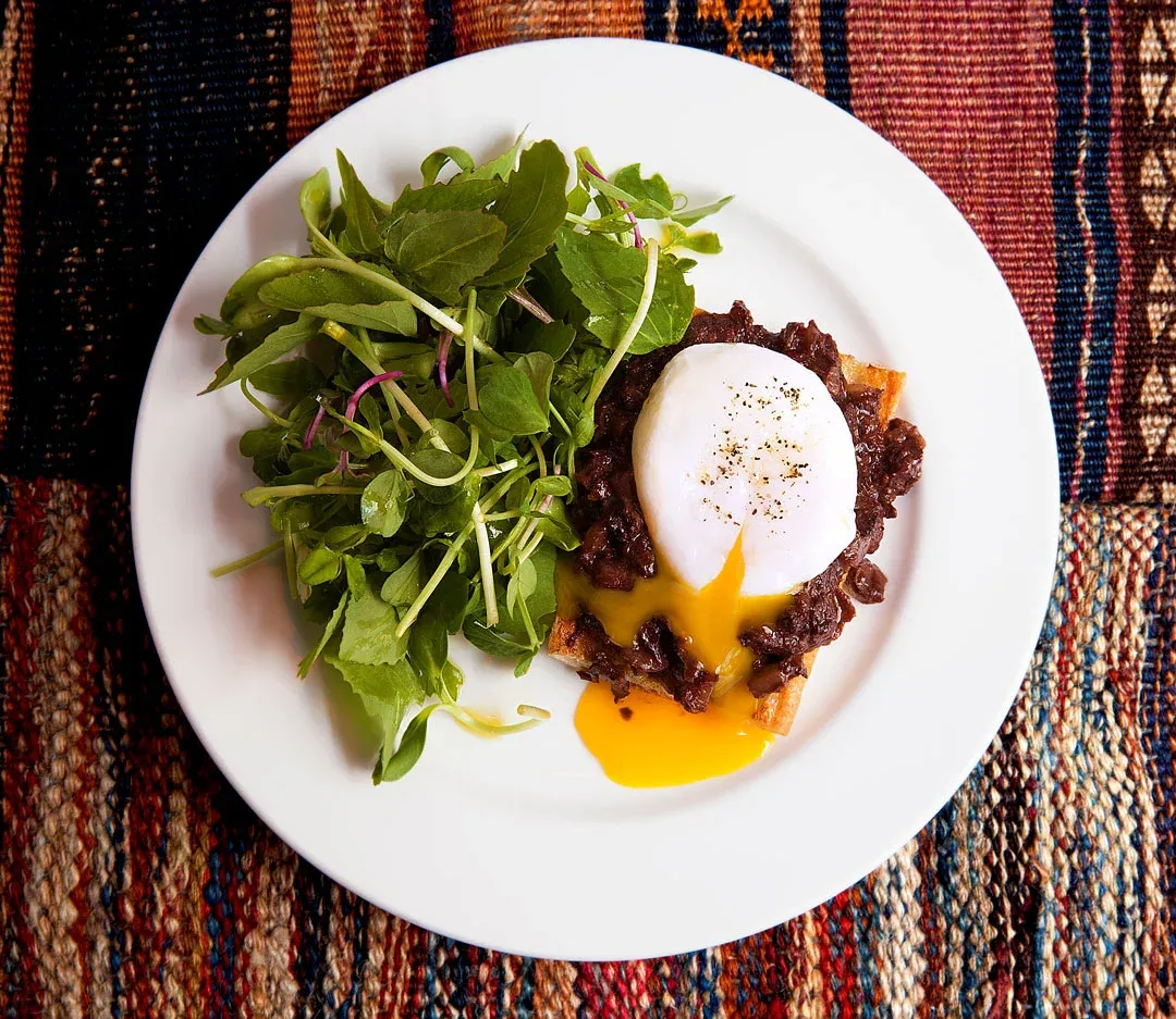 Poached egg with rich brown sauce and greens on toast.