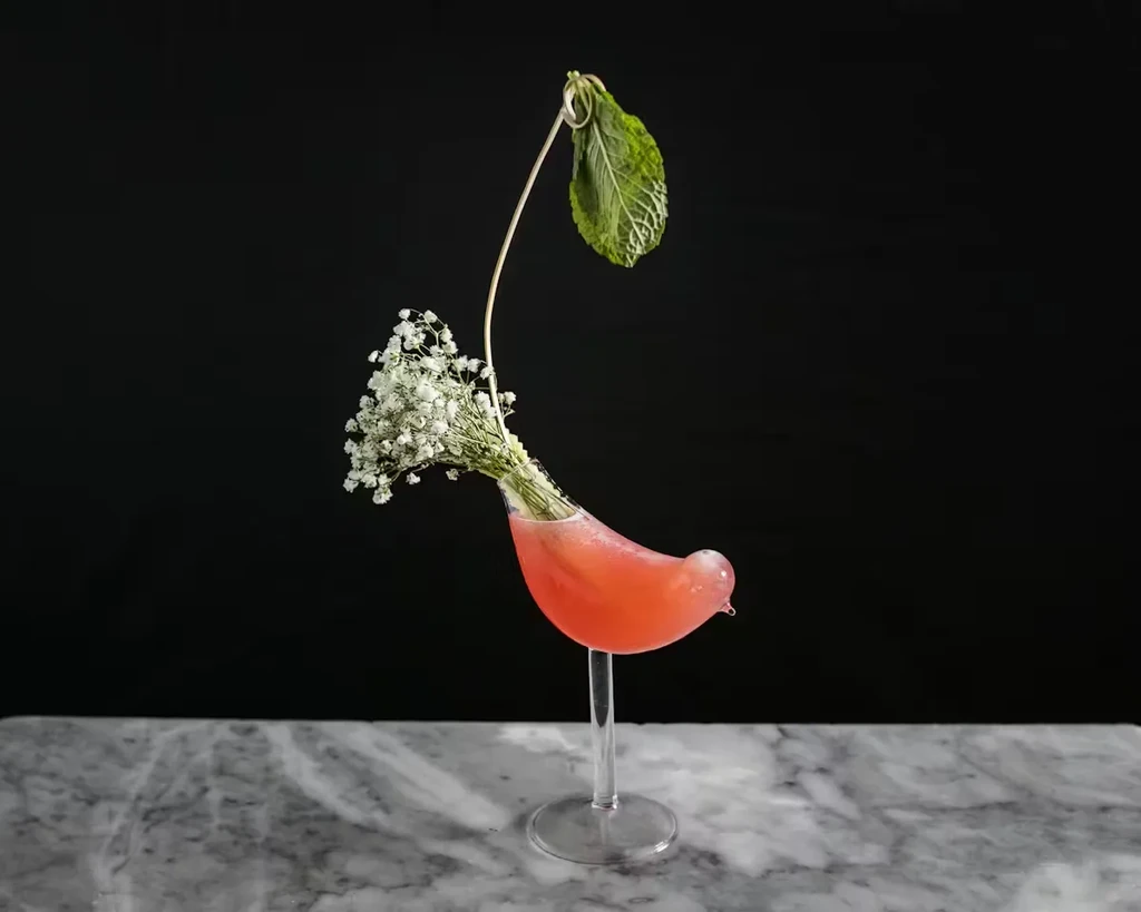 Bird-shaped glass with pink drink, baby's breath, and mint leaf.