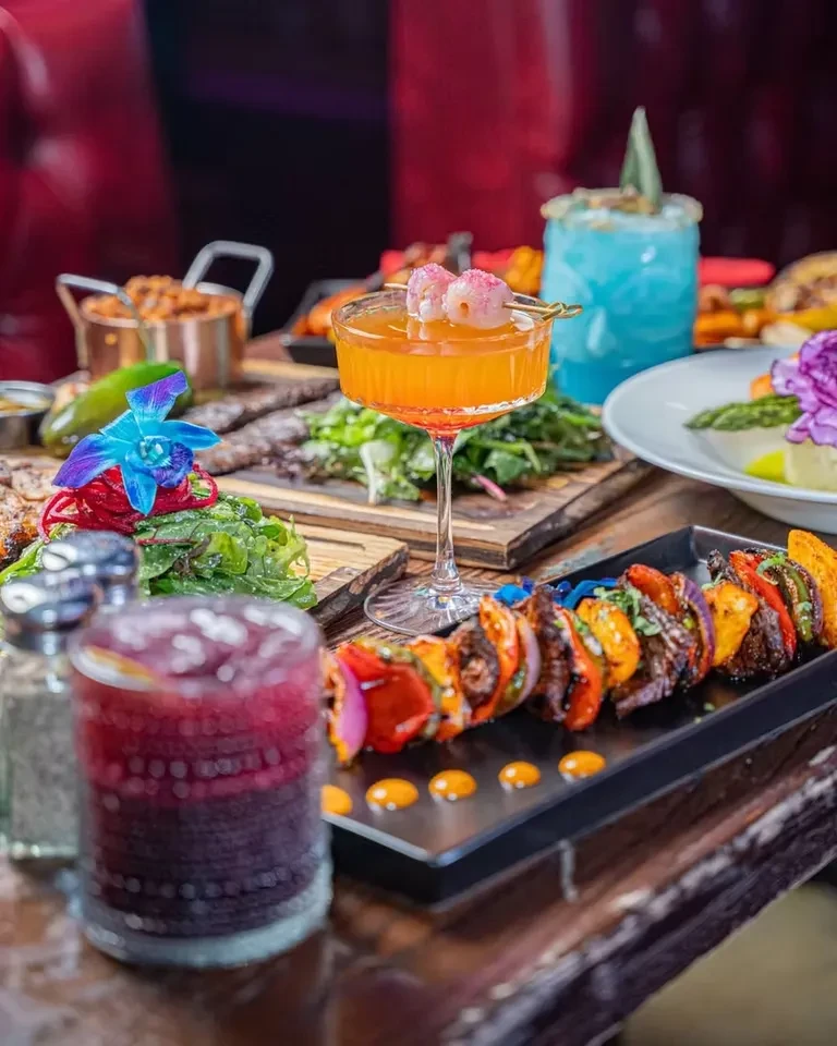A table laden with cocktails, skewers, salad, and other dishes.