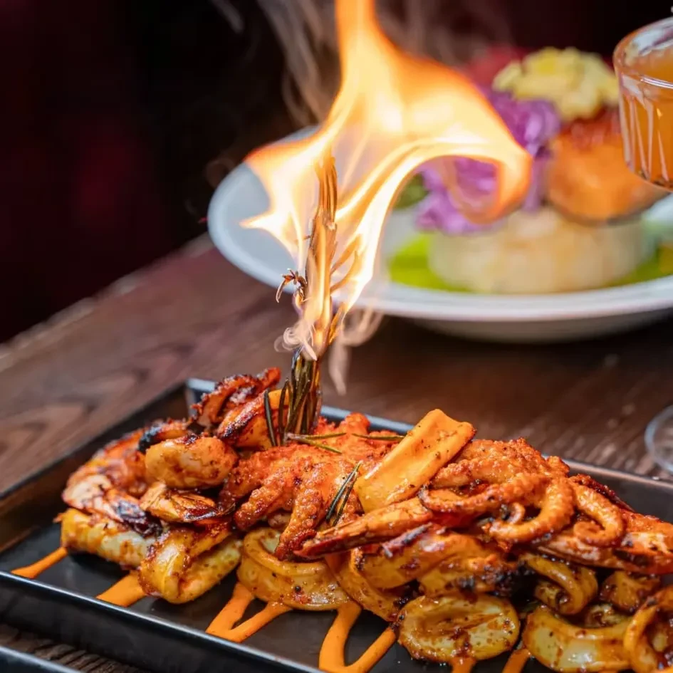 A flaming dish of prawns and calamari on a black plate.