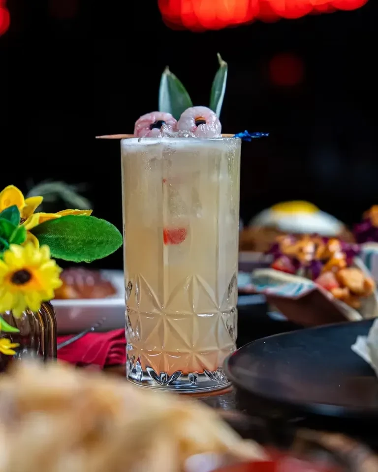 A tall, patterned glass cocktail garnished with lychees and green leaves.
