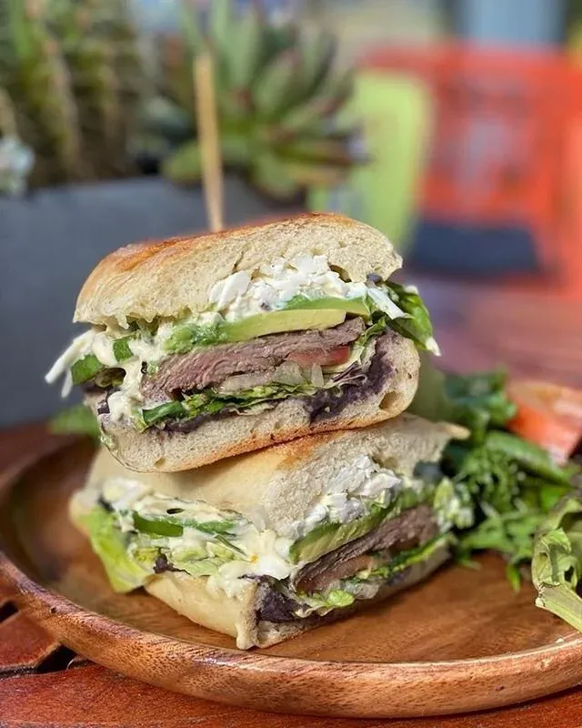 A steak sandwich, halved and stacked on a wooden plate.