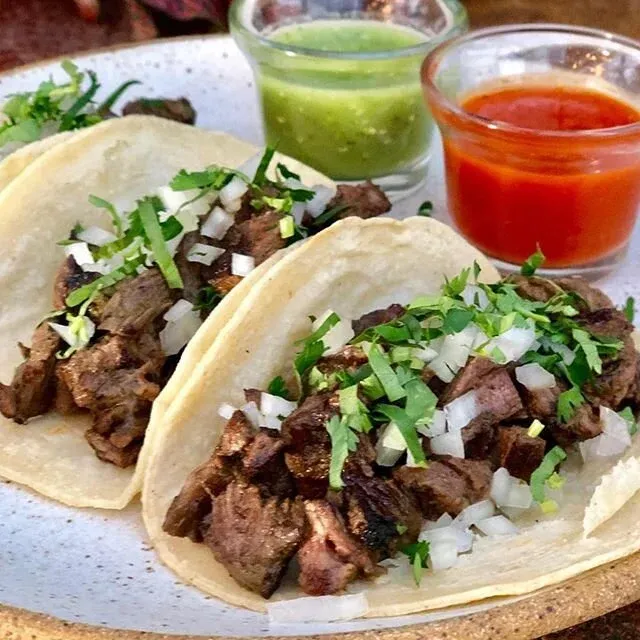 Three tacos with chopped meat, onion, cilantro, green and red salsa.