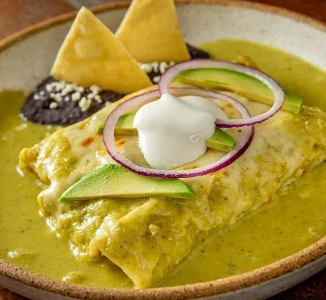 Enchiladas with green sauce, sour cream, avocado, onions, and tortilla chips.