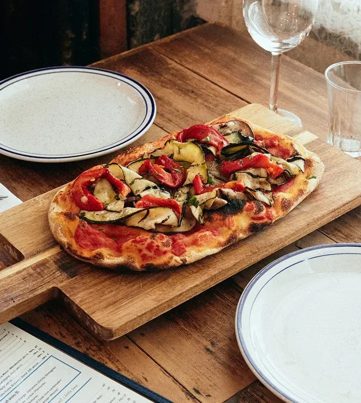 A rectangular vegetable pizza on a wooden board at a restaurant table.