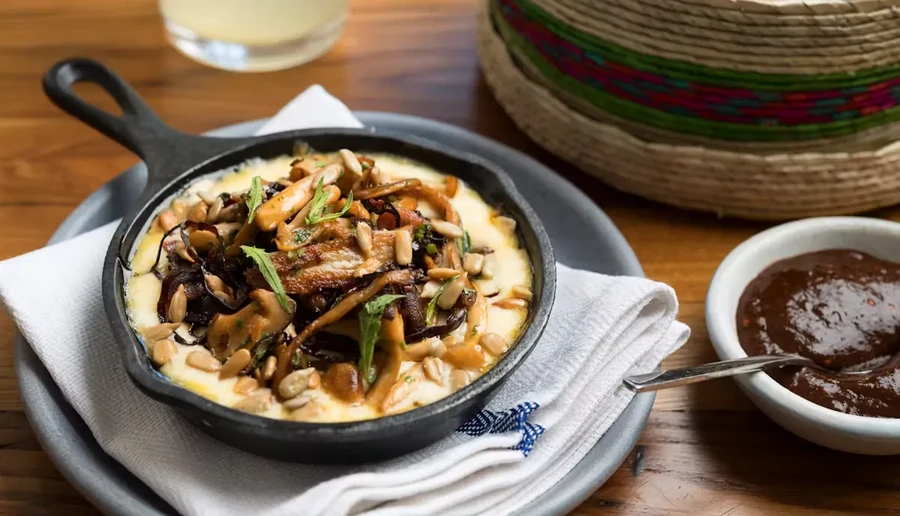 Skillet of melted cheese topped with mushrooms, onions, seeds, and sauce.