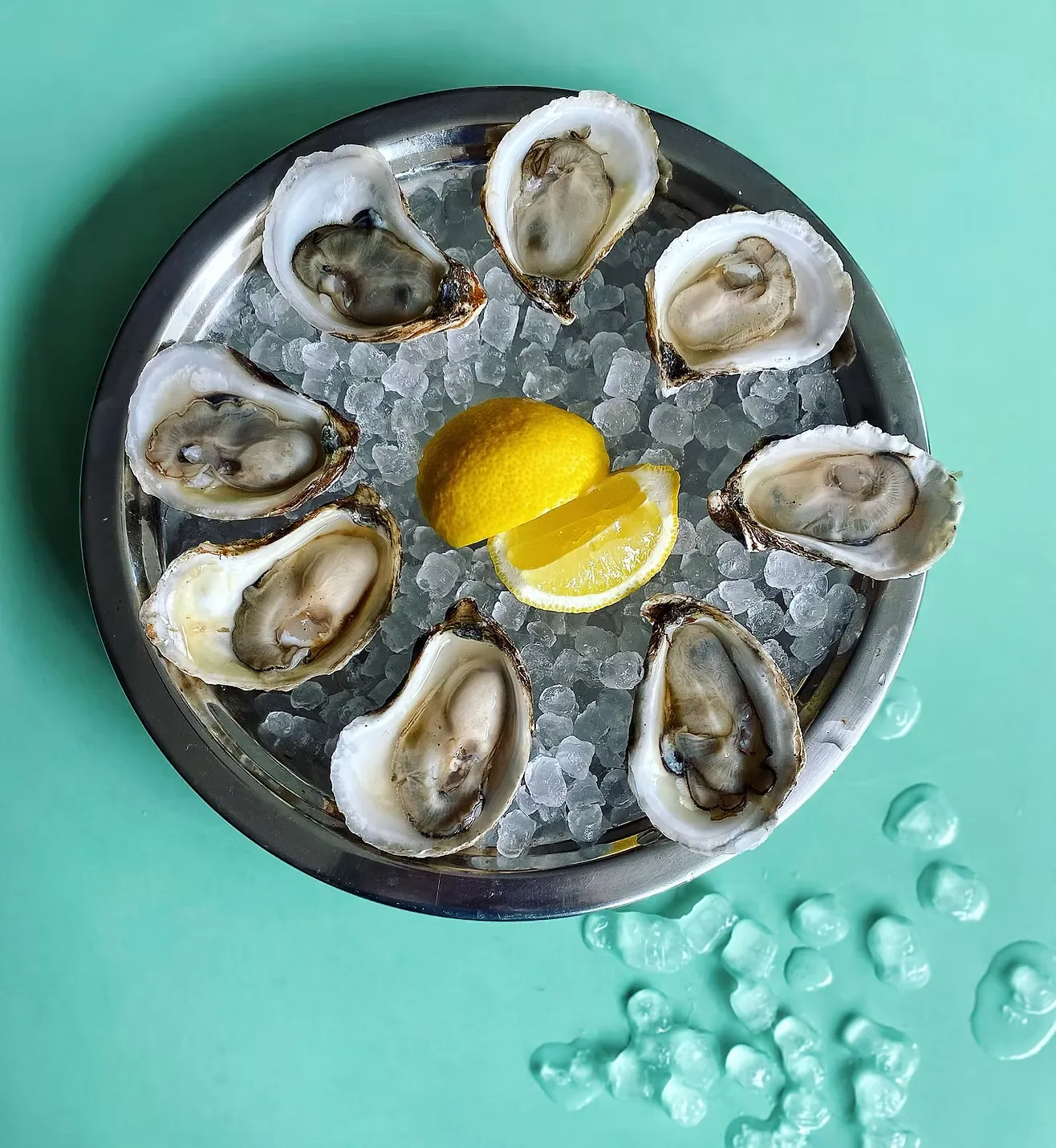 Nine oysters on ice with lemon slices on a metal tray.