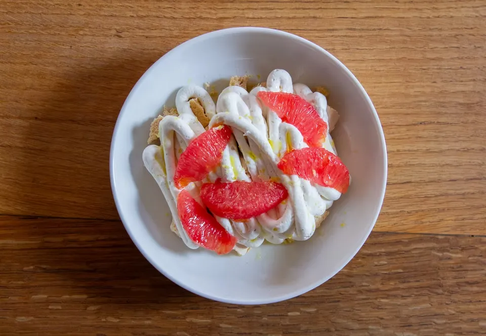 A white bowl of grapefruit segments, cream, and cake on wood.
