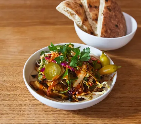 Bowl with chicken, coleslaw, pickles, peppers, and pita bread.