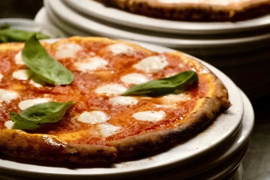 A stack of pizzas on white plates, basil and mozzarella visible.