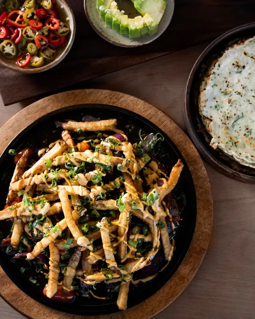 Fries topped with sauce and scallions on a black skillet.