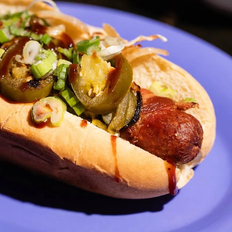 A hot dog in a bun, topped with jalapenos and scallions.
