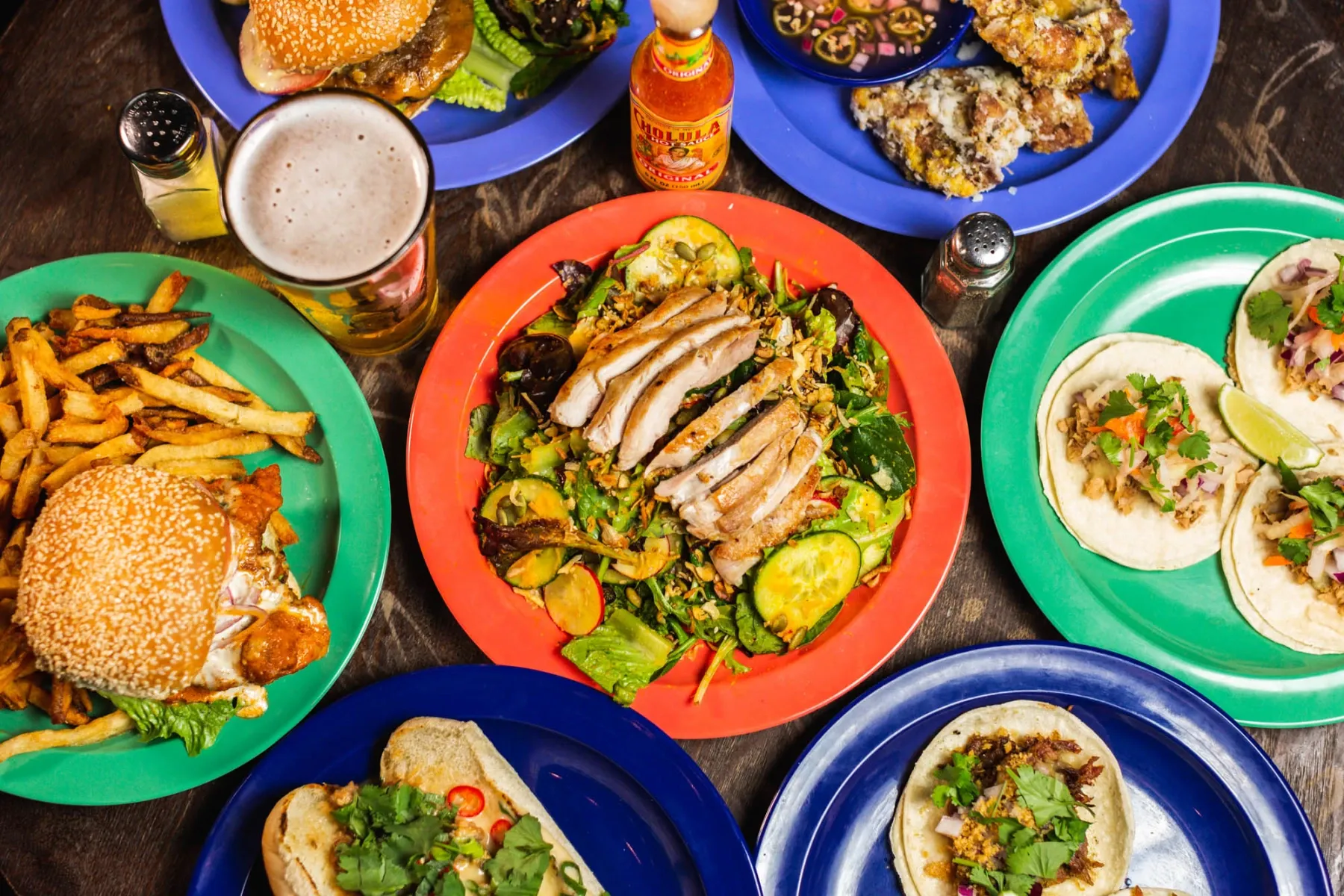 Assortment of food plates including burgers, tacos, salads, and a beer.