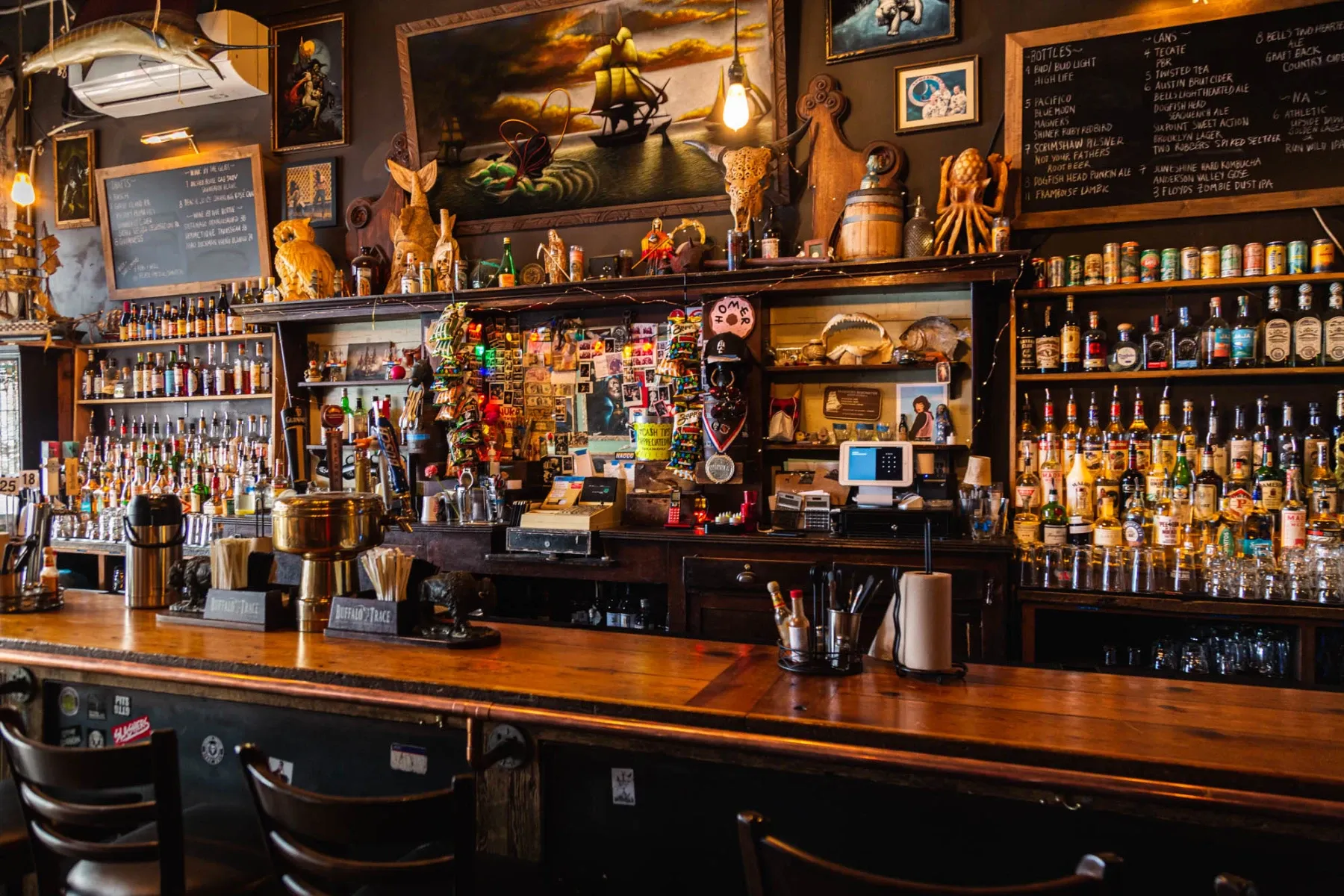 A cluttered bar with liquor bottles, artwork, and various decorations.