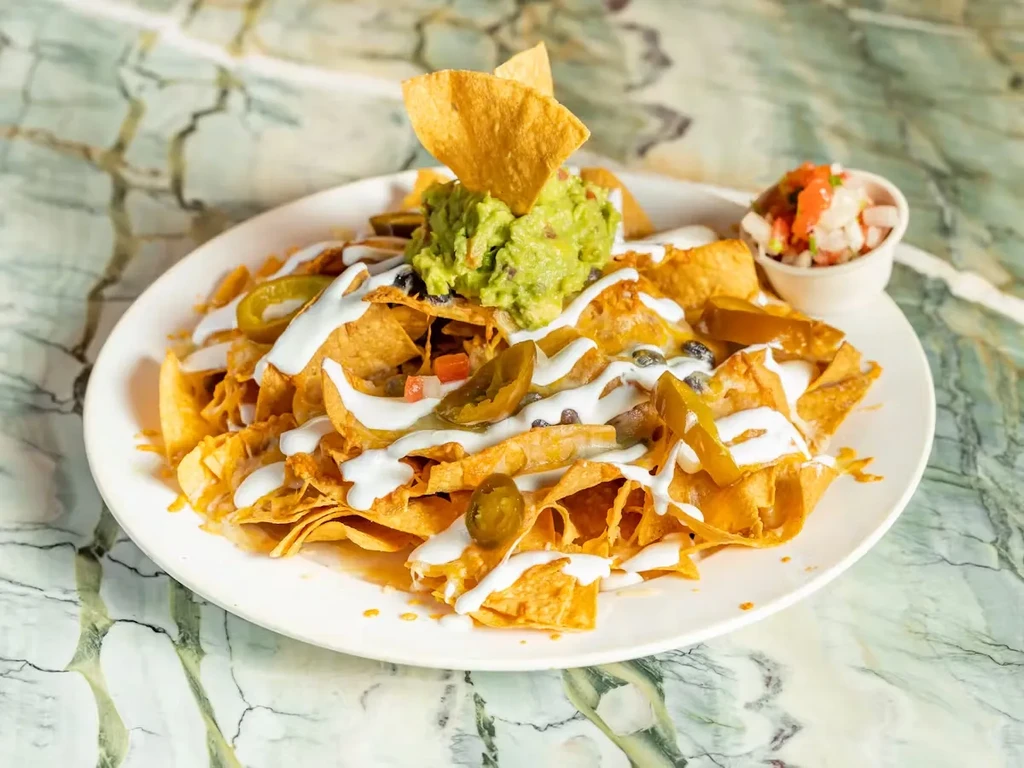 Plate of nachos with guacamole, sour cream, and jalapeños.