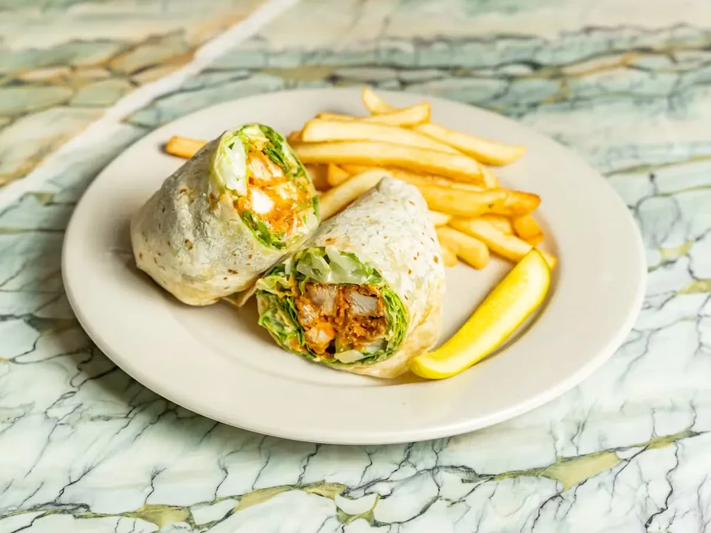 Two chicken wraps, fries, and a pickle on a white plate.