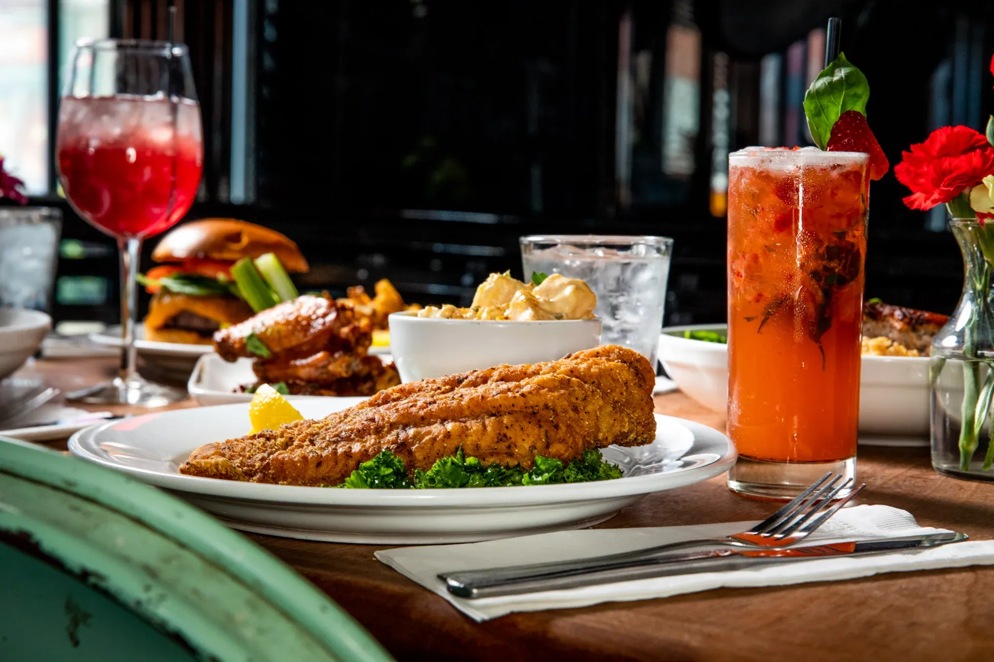A restaurant table with a fried fish entree and red drinks.