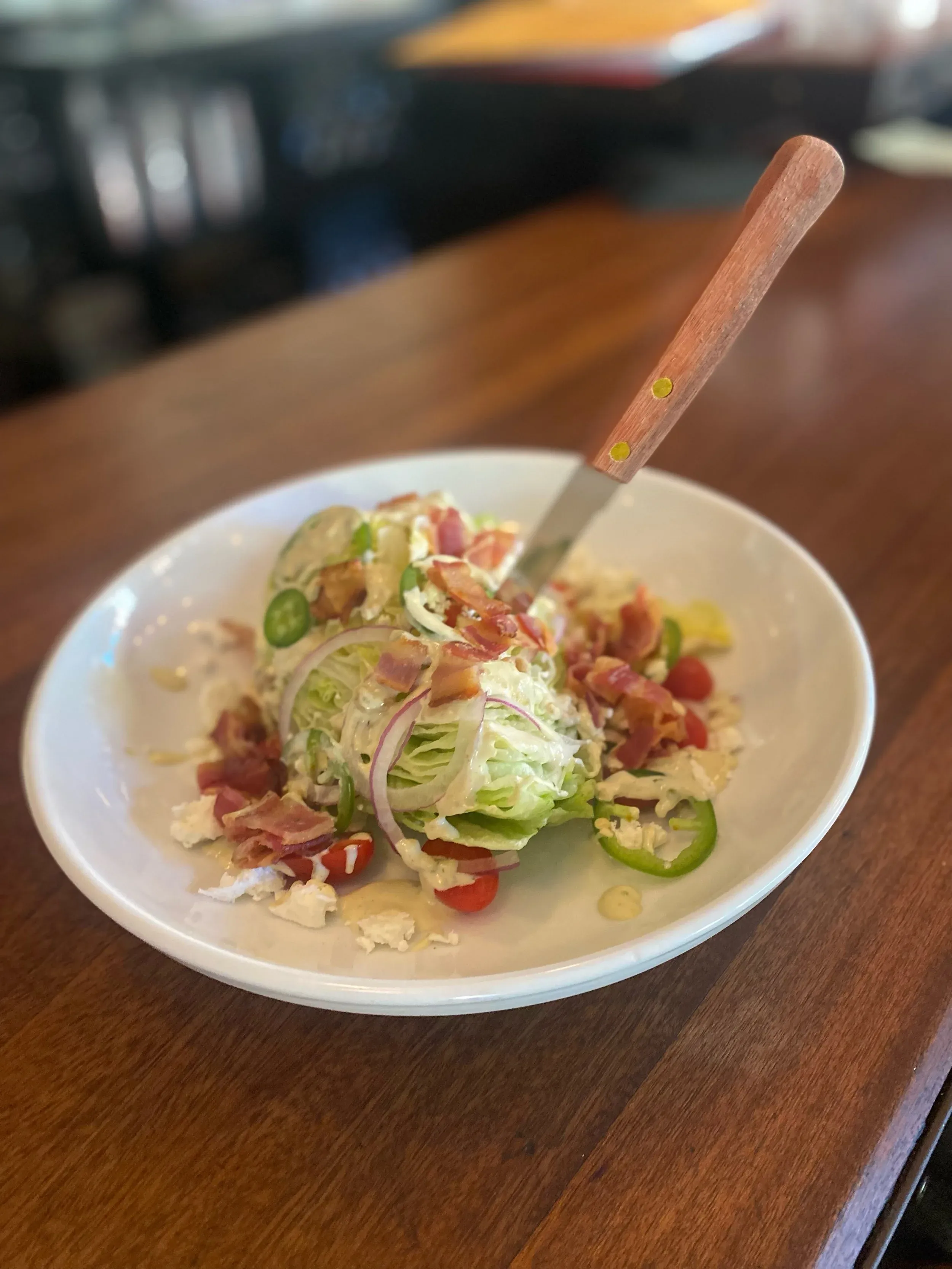 Wedge salad with bacon, tomatoes, and dressing, on a white plate.